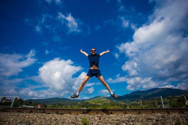 adam bir çim tepe ufuk çizgisinin üstündeki üzerinde sevinç için atlama. Tek bir mutlu ince insan sinek mavi yaz göğün bulutları ve dağ karşı yeşil bir alanda