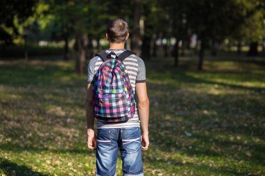 Gün batımı arkadan görünüm, sırt çantası ile park önünde duran genç adam