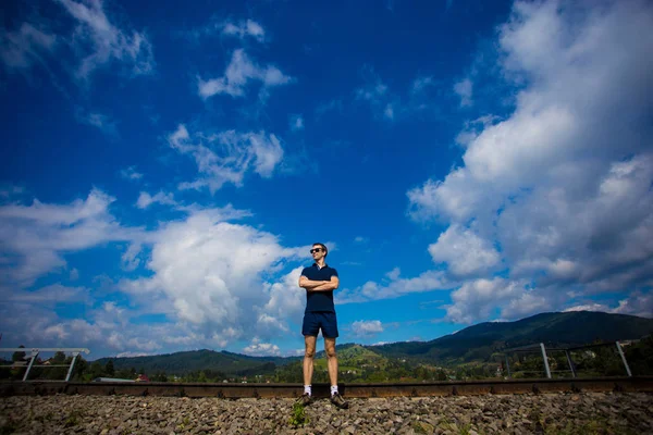 Güneş gözlüklü genç çekici adam mavi gökyüzüne karşı duruyor