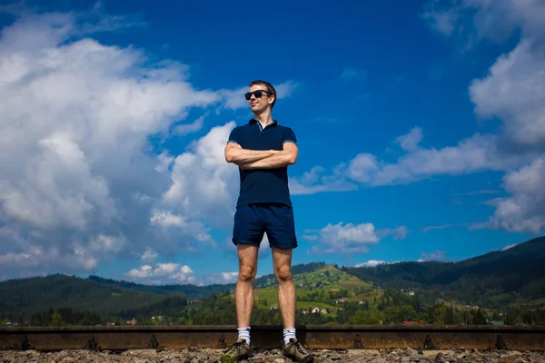 Güneş gözlüklü genç çekici adam mavi gökyüzüne karşı duruyor