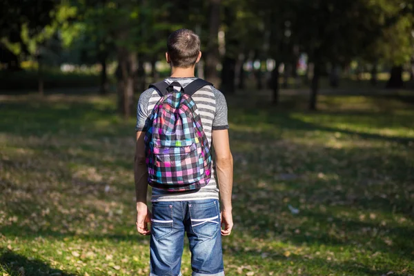 Gün batımı arkadan görünüm, sırt çantası ile park önünde duran genç adam