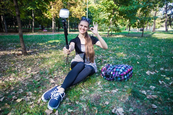 Çimenlerin üzerinde oturan ve selfie üzerinde bir eylem fotoğraf çekici genç güzel kız