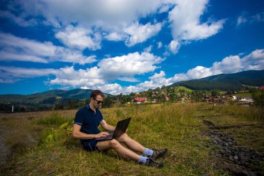 Genç adam dizüstü bilgisayarla oturuyor.