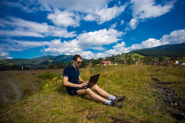 Genç adam dizüstü bilgisayarla oturuyor.