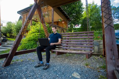 Genç adam dizüstü bilgisayarla oturuyor.