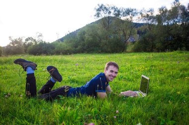 Genç adam yalan dizüstü bilgisayar ve çalışma yeşil çimenlerin üzerinde 