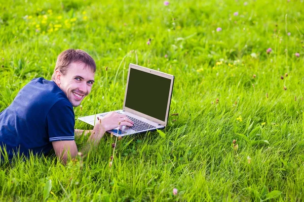 Genç adam yalan dizüstü bilgisayar ve çalışma yeşil çimenlerin üzerinde 