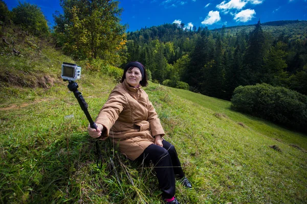 Счастливая пожилая женщина сидит на вершине холма и наслаждается видом на горы — стоковое фото