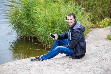 Genç adam ruhları nehir kıyısında bir telefon ile oturur ve müzik dinliyor
