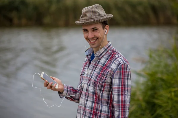 Bir telefon ile modern giyimleri genç gülümseyen adam müzik dinliyor