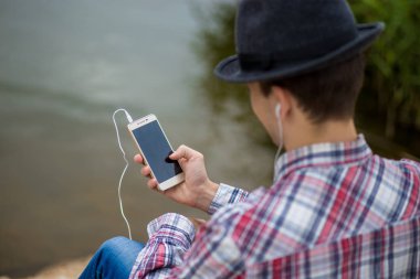 Bir telefon ile modern giyimleri genç gülümseyen adam müzik dinliyor