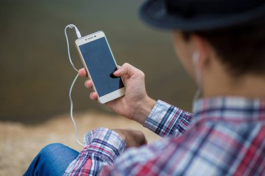Bir telefon ile modern giyimleri genç gülümseyen adam müzik dinliyor