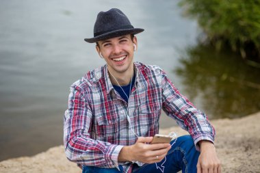 Bir telefon ile modern giyimleri genç gülümseyen adam müzik dinliyor