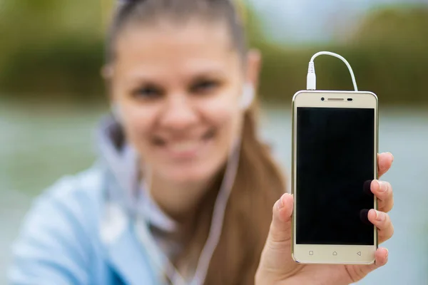 Young smiling woman in excellent spirits with a phone listens to music — Stock Photo, Image