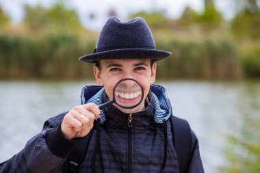 Büyüteç bir şapka komik bir yüz ile neşeli bir adam tutar