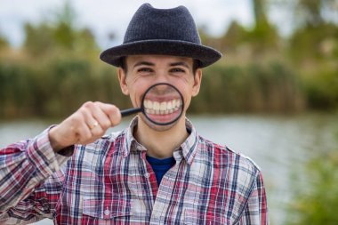 A cheerful man with a funny face in a hat holds a magnifying glass clipart