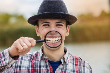 Büyüteç bir şapka komik bir yüz ile neşeli bir adam tutar