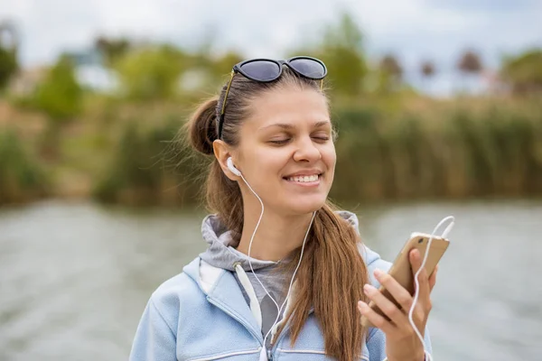 Giovane donna sorridente di ottimo umore con un telefono ascolta la musica — Foto Stock