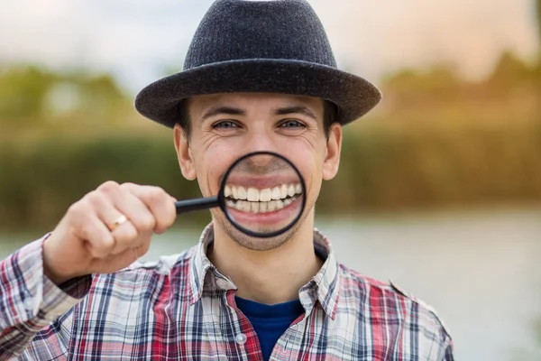 Büyüteç bir şapka komik bir yüz ile neşeli bir adam tutar