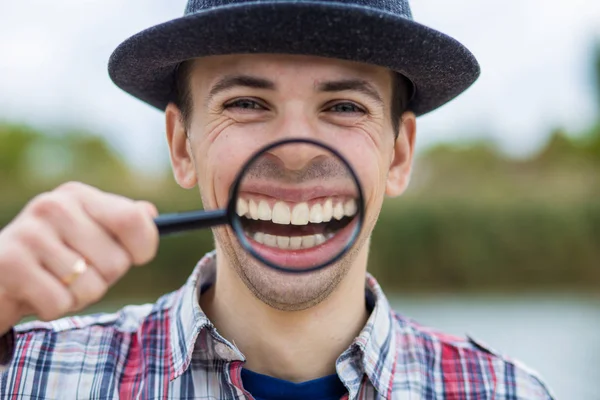 Büyüteç bir şapka komik bir yüz ile neşeli bir adam tutar