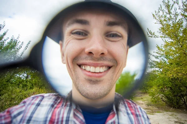 Büyüteç bir şapka komik bir yüz ile neşeli bir adam tutar