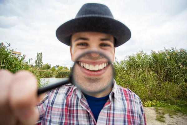 Büyüteç bir şapka komik bir yüz ile neşeli bir adam tutar