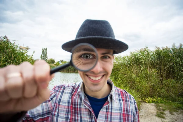A cheerful man with a funny face holds a magnifying glass