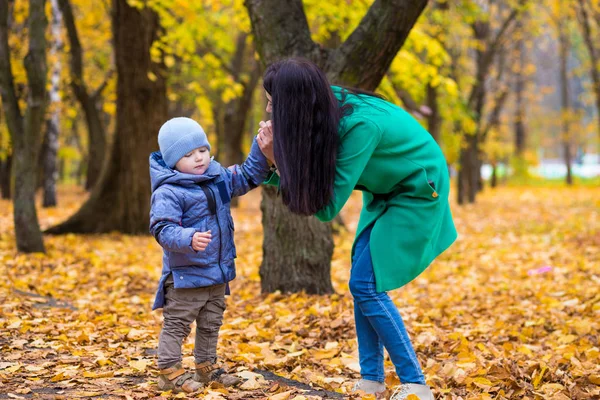 Madre con hijo pequeño se para en el parque sobre el fondo de las hojas de otoño —  Fotos de Stock