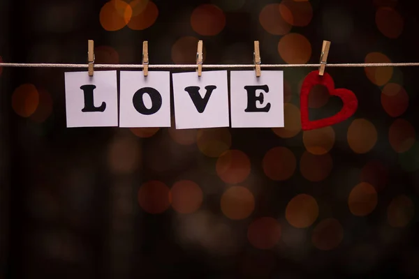 Texto de amor en papeles con pinzas de ropa con guirnalda bokeh en el fondo —  Fotos de Stock