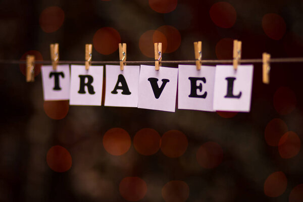 Travel text on papers with clothespins with garland bokeh on background. The word 
