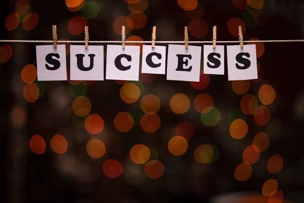 Success text on papers with clothespins with garland bokeh on background
