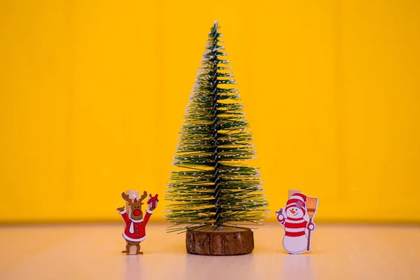 Decorative Christmas tree with funny deer and snowman on table with yellow background
