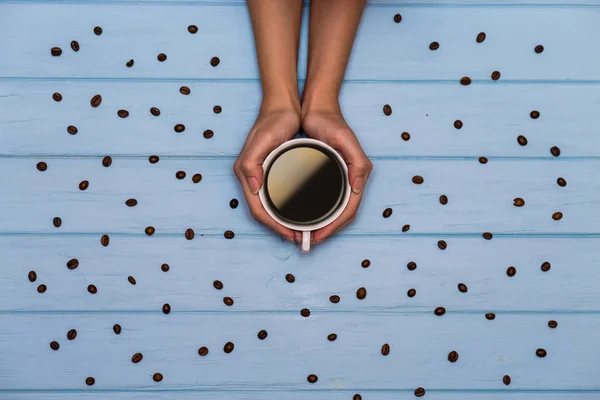 女性の手は青い木製のテーブルの周りの多くのコーヒー豆とコーヒーのキャップを保持する 上記表示 — ストック写真