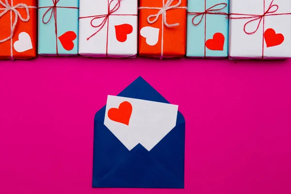 Love letter in blue envelope on pink background with bright gift boxes. Love concept