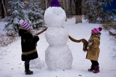 Küçük bir neşeli kızlar bir eşarp için büyük bir kardan adam koymak. Sevimli küçük kız kardeşi var. eğlenceli kış Park, kış