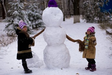 Küçük bir neşeli kızlar bir eşarp için büyük bir kardan adam koymak. Sevimli küçük kız kardeşi var. eğlenceli kış Park, kış
