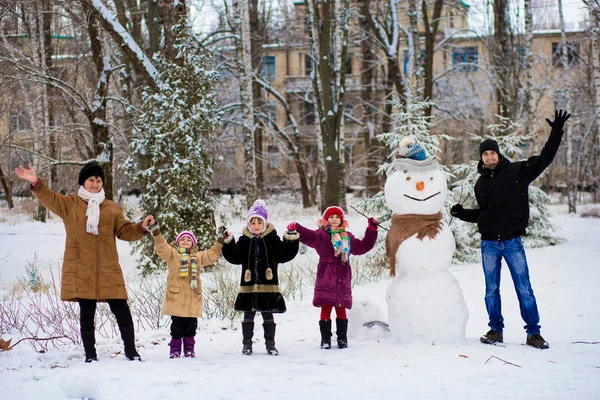 Big happy family: father, daughters and grandmother sculpt a big real snowman, Happy family have fun in a winter park