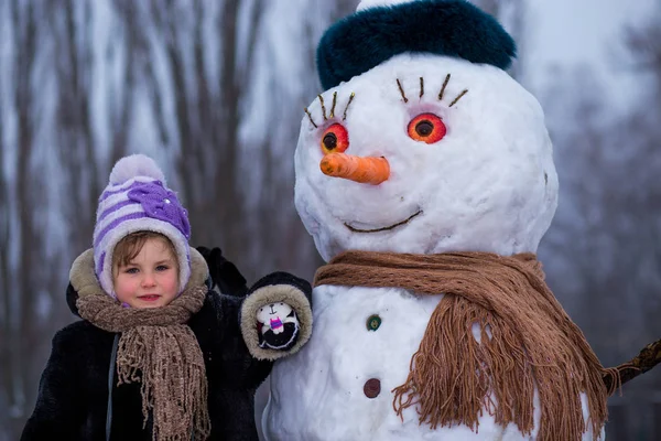 Маленькая Весёлая Девочка Сидит Рядом Большим Настоящему Смешным Снеговиком Симпатичная — стоковое фото