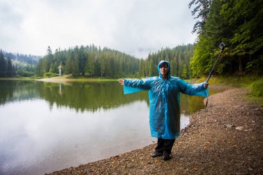 Mutlu kadın turist 60 yaşında büyük dağ Gölü'nün güzel manzarayı yağmurluk. Üst düzey turist kadının yanına selfie eylem kamera, uyum kavramı alarak Orman Gölü