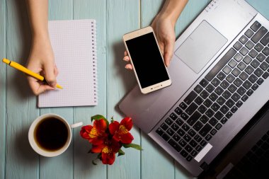 bilgisayar kullanma ve yazma telefon ile boş defter, laptop, fincan kahve ve çiçekler ile Modern beyaz ofis resepsiyon masası üzerinde kadın iş ver. Üstten Görünüm, düz yatıyordu. İş analizi ve strateji kavramı.