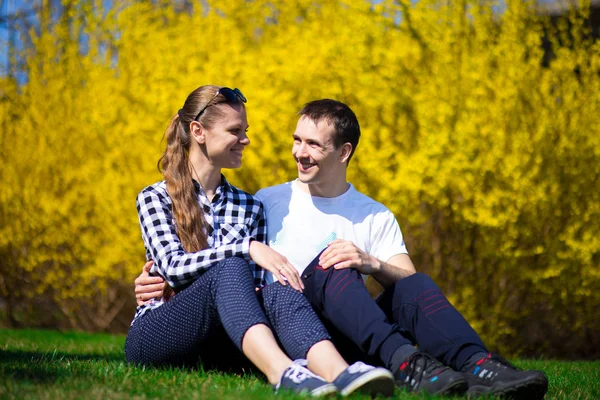 Couple in love hug in park on fresh green grass near tree in yellow blossom. Spring time.
