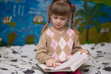 Küçük neşeli kız yatakta kitap okuyun. Çocuklar bilgi kavramı