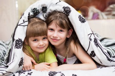 Komik little sisters battaniyenin altında gizler. Şirin kızlar yatakta eğleniyor. Çocuklar uyku, bakım veya çocukluk kavramı