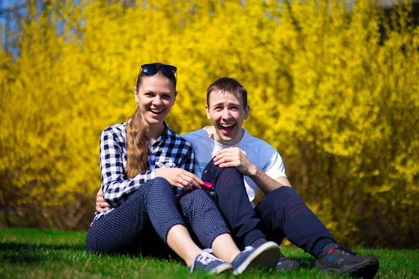Couple in love hug in park on fresh green grass near tree in yellow blossom. Spring time