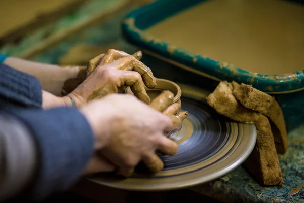 セレクティブ フォーカスから花瓶を作るエプロンの陶工の手でクローズ アップ 一緒になっています 陶器のホイールに陶磁器の鍋をする子供を教える ポッターの平面図 — ストック写真