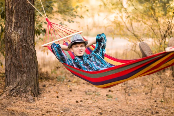 Joven feliz hombre libre en sombrero relajante al aire libre en hamaca en el bosque — Foto de Stock