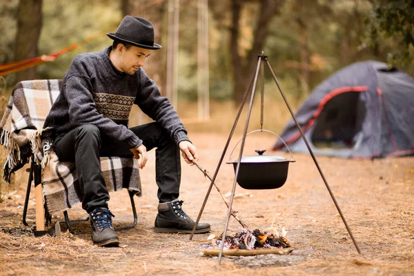Young man camping in tent on autumn and cook food on campfire. Vacation Concept