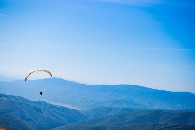 Dağ tepelerinde uçan siluet, arka planda dağ vadisi.