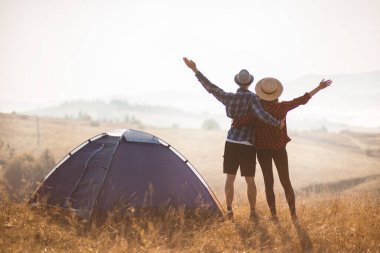 Sevgi dolu çiftlerin silueti sonbahar tatilinde kamp kurar. Elleriniz havada güneşin doğuşunun tadını çıkarın..