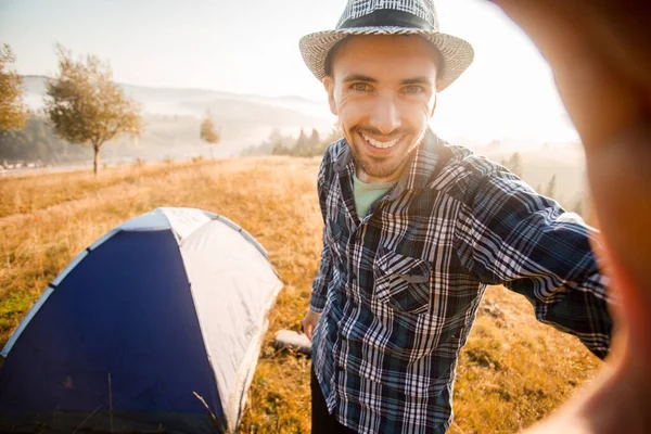 Fanny hombre barbudo sonriendo y tomando selfie en las montañas desde su teléfono inteligente. Hombre viajero con barba usando sombrero tomar autorretrato con cámara después del senderismo de otoño . —  Fotos de Stock